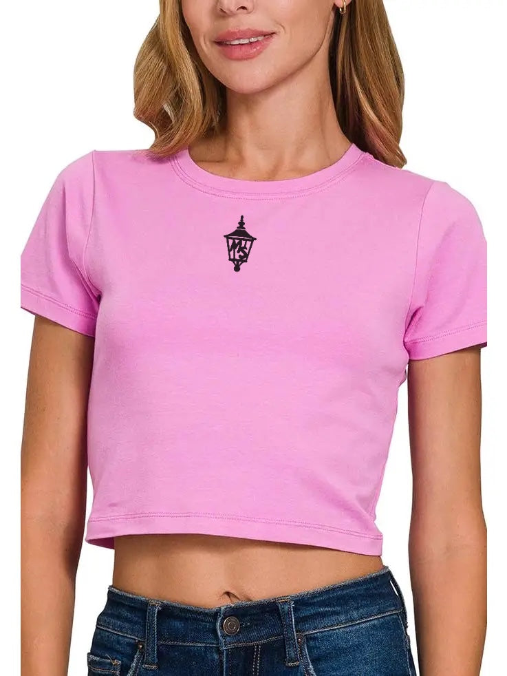 Person wearing a pink crop top with a black logo and blue jeans on a white background